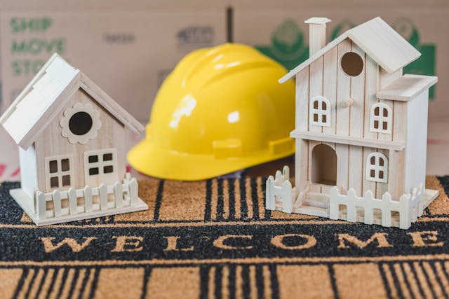 Miniature Houses Beside a Hard Hat on  Welcome Sign